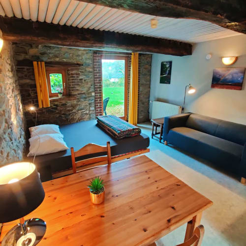 Studio cosy au rez-de-chaussée à La Ferme De Werpin avec lit, coin salon, table en bois et vue sur le jardin