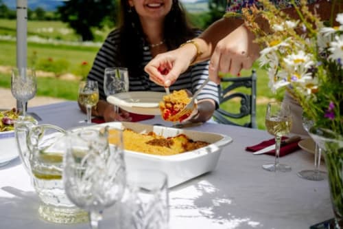 Femme servant un déjeuner en terrasse au Château de Vaux Morvan à Étang sur Arroux avec vue sur le jardin et verres de vin