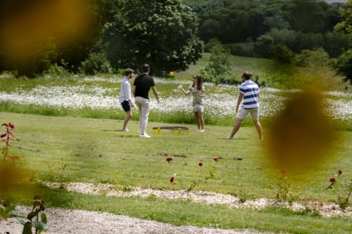 Des invités jouent au cornhole dans le jardin du Château de Vaux Morvan, avec des fleurs sauvages et des arbres en arrière-plan