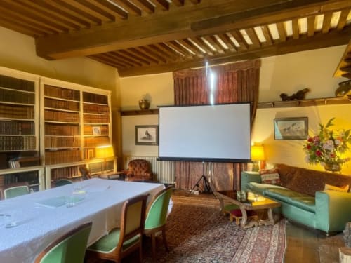 Salle de conférence du Château de Vaux Morvan avec écran de projection, poutres en bois, bibliothèques et table de réunion