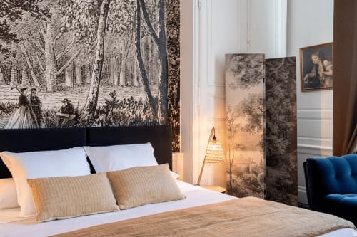 Elegant bedroom at Henri II hotel in Le Mans with forest mural headboard, white bedding, and decorative artwork
