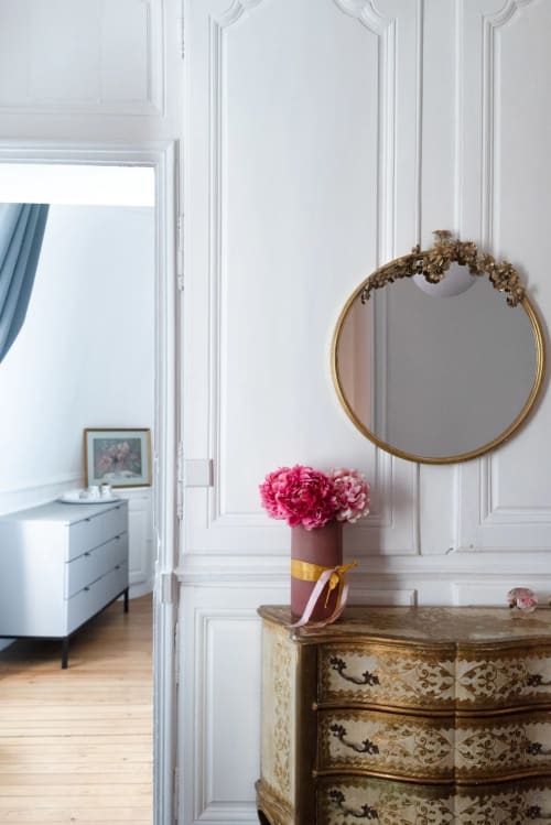 Elegant room at Henri II hotel in Le Mans featuring pink peonies in a vase on an ornate dresser, with a gold circular mirror