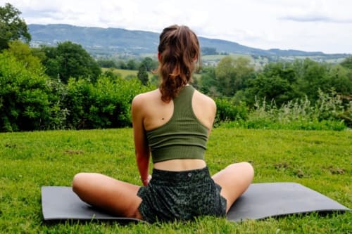 Femme en méditation sur son tapis de yoga en plein air face à la campagne près du Château de Vaux Morvan, Étang-sur-Arroux, France