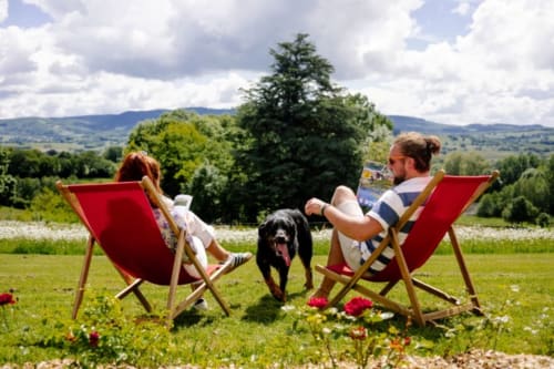 Couple relaxing in red deck chairs with dog overlooking Morvan countryside near Étang sur Arroux
