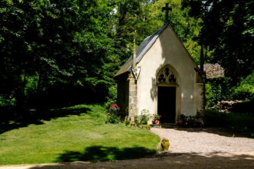 Small white chapel with cross nestled in lush green grounds at Château de Vaux Morvan, Étang sur Arroux