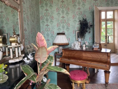 Élégant salon du Château de Vaux Morvan avec papier peint damassé, piano en bois et décor aux accents roses
