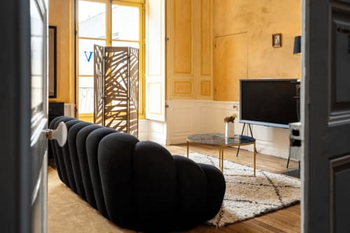 La suite Marquis de l'hôtel Henri II au Mans dispose d'un canapé sculptural noir moderne, d'une télévision écran plat et d'une élégante