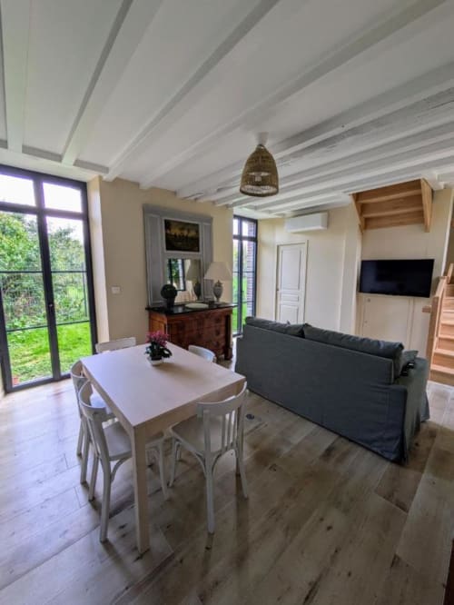 Open-plan living area at Manoir Saint Joseph with dining table, grey sofa, and garden views in Sens