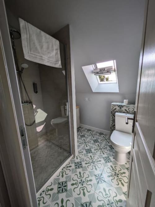 Modern bathroom in Manoir Saint Joseph villa with walk-in shower, toilet, sink, patterned tiles, and skylight window