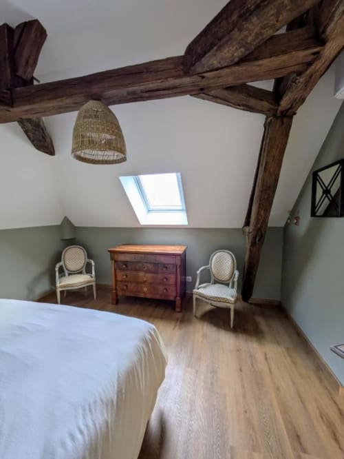 Rustic attic bedroom at Manoir Saint Joseph with exposed wooden beams, skylight, period chairs, wooden chest, and white