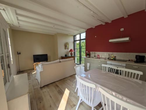 Open-plan kitchen and living area in Manoir Saint Joseph villa with red accent walls, dining table, sofa, and garden views