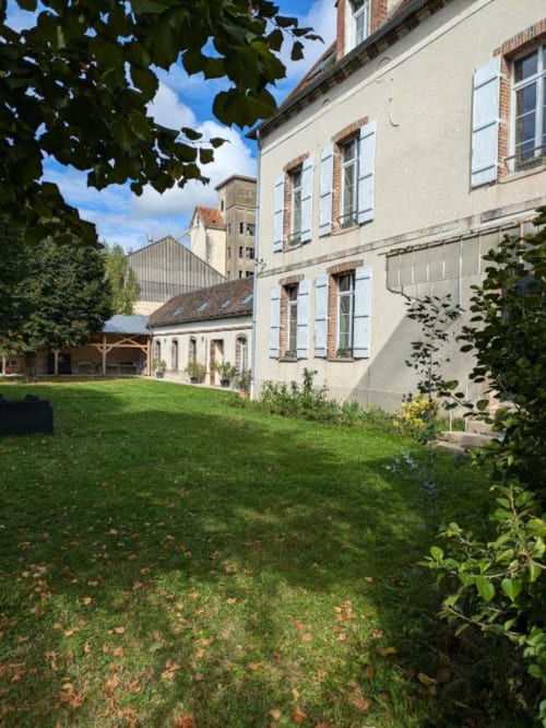 Manoir Saint Joseph guest house garden in Sens with lawn, ivy-covered building facade, and stone structures