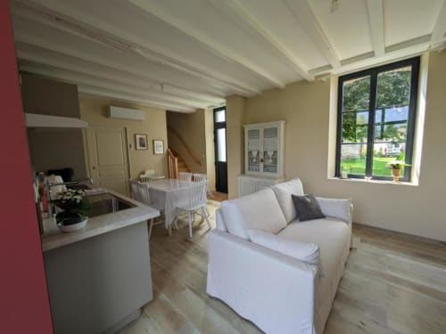 Bright open-plan living area in Manoir Saint Joseph villa with cream sofa, dining table, kitchen, exposed beams, and garden