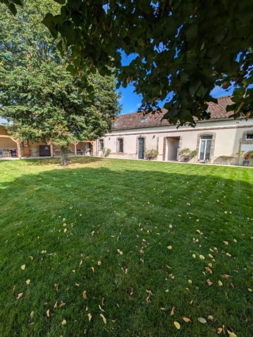 Manoir Saint Joseph guest house courtyard in Sens with manicured lawn, mature trees, and cream-colored villa building with