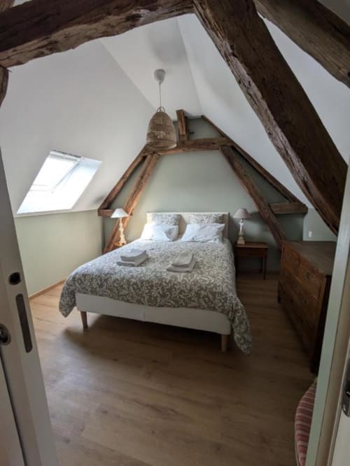 Attic bedroom at Manoir Saint Joseph in Sens with exposed wooden beams, skylight, queen bed with patterned bedding, and