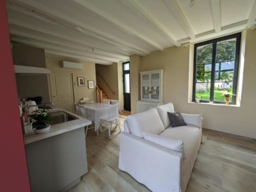 Bright open-plan living room and kitchen at Manoir Saint Joseph hotel in Sens, with white sofa, dining table, and large