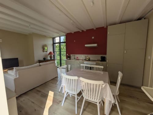 Open-plan living area at Manoir Saint Joseph villa with dining table, white chairs, kitchen with red accent wall, and garden