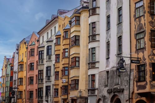 Fachadas de edificios históricos con colores vibrantes y ventanas ornamentadas en una calle europea bajo un cielo azul.