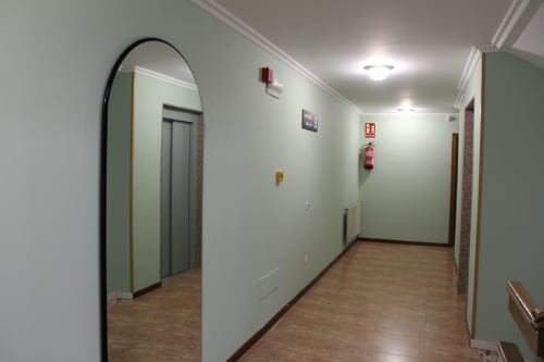 Pasillo del Hotel Rego Foz con ascensor, paredes verde pálido, suelo de madera y espejo arqueado en Foz, Lugo