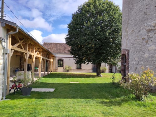 Cour de la maison d'hôtes Manoir Saint Joseph à Sens avec pelouse verdoyante, pergola en bois et bâtiments historiques en pierre