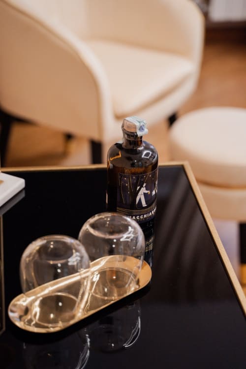 Lussuosi amenities di benvenuto a Villa Del Sole Inn, Campobasso: bottiglia di vetro scuro, bicchieri trasparenti e vassoio dorato su superficie nera