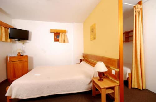 Chambre d'hôtel lumineuse aux murs jaunes, mobilier en bois, literie blanche, télévision et vue sur les montagnes aux Hôtel Studios La