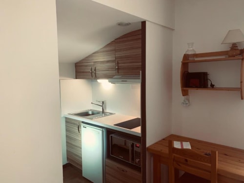 Kitchenette compacte en studio à Brides-les-Bains avec placards bois, évier, micro-ondes et coin repas
