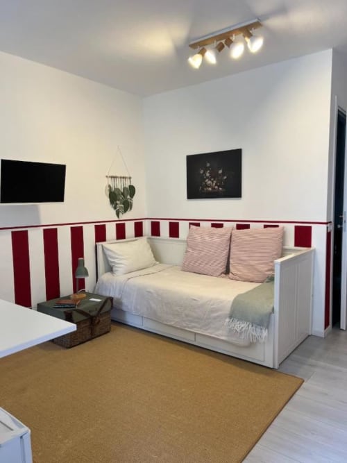 Modern bedroom at La Cascina di Bea B&B with white bed, red and white striped wallpaper, wooden flooring, and garden view.