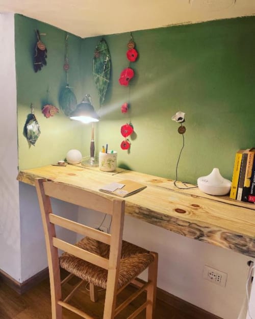 Cozy desk workspace at La Cascina di Bea with wooden desk, lamp, and green walls decorated with hanging flowers.