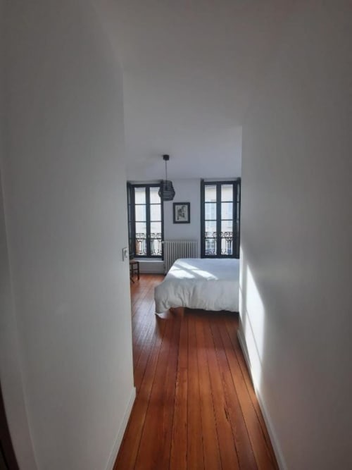 Couloir lumineux de la chambre à Maison Rinette, Dijon, avec parquet, lit et vue sur la ville par portes à cadre noir