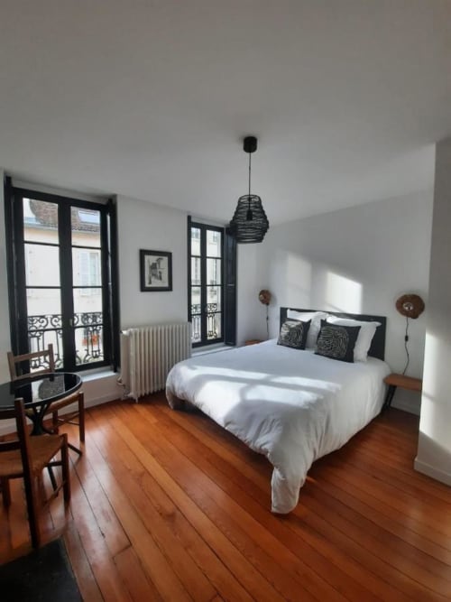 Chambre lumineuse à la Maison Rinette B&B à Dijon avec literie blanche, parquet, fenêtres à cadre noir et luminaire suspendu