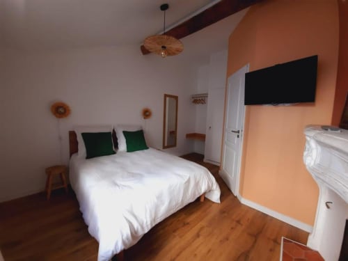 Chambre Maison Rinette à Dijon : lit blanc, oreillers verts, murs pêche, parquet, TV et suspension.