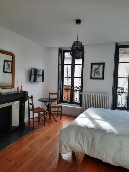Chambre élégante à la Maison Rinette Dijon avec parquet, portes-fenêtres vue sur la ville, cheminée et suspension moderne noire