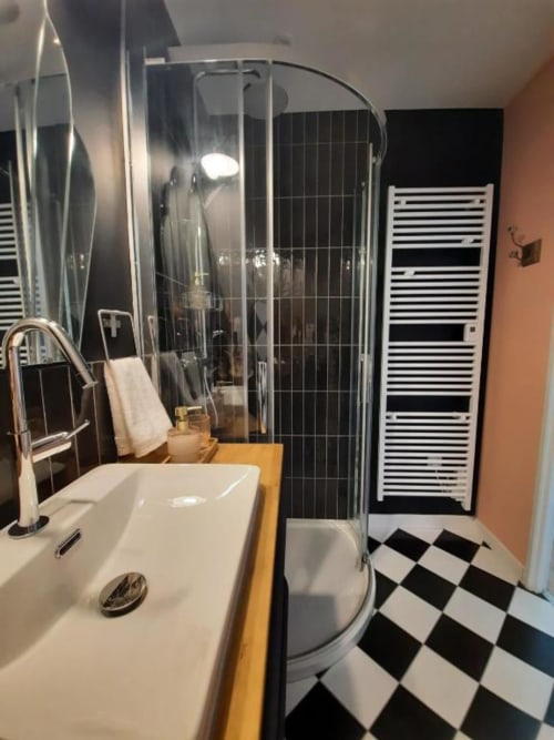 Salle de bains moderne de la Maison Rinette B&B à Dijon avec lavabo blanc, carrelage damier noir et blanc, et douche vitrée.