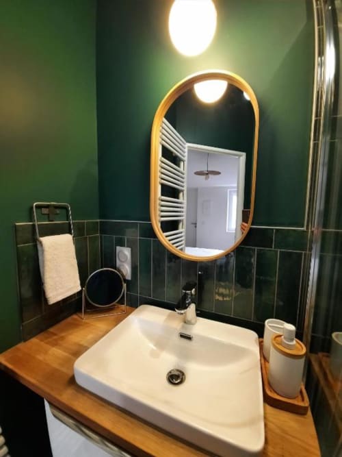 Salle de bain moderne à la Maison Rinette B&B à Dijon avec carrelage vert, meuble-lavabo en bois, lavabo blanc et miroir ovale illuminé