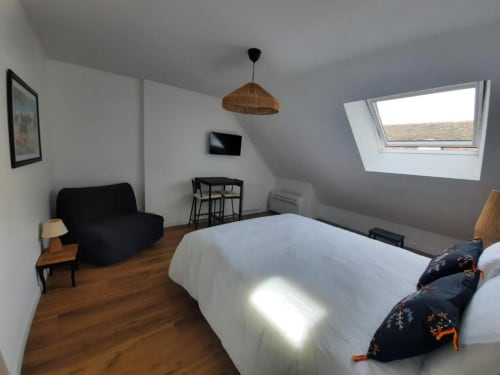 Chambre mansardée moderne à la Maison Rinette à Dijon avec lit queen-size, fenêtre de toit, canapé noir et parquet