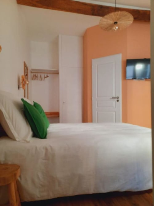 Chambre moderne à la Maison Rinette B&B à Dijon avec murs pêche, lit blanc, coussin vert et télévision écran plat