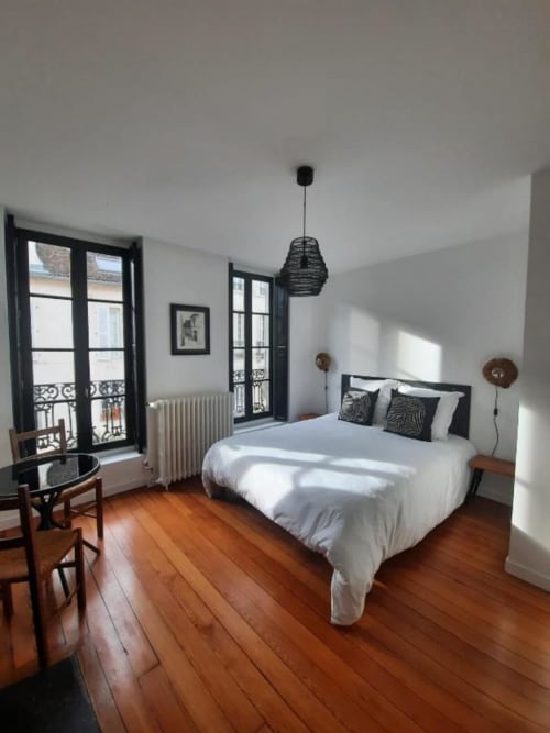 Chambre lumineuse à la Maison Rinette à Dijon avec parquet, portes donnant sur la ville, literie blanche et luminaire suspendu moderne