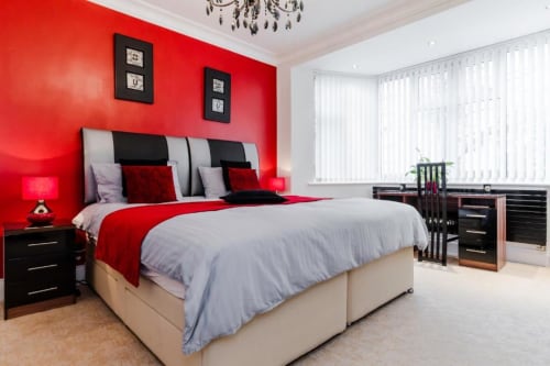 Modern king bedroom at Brooklyn House with bold red walls, grey bedding, black furniture, and garden views in Southgate,