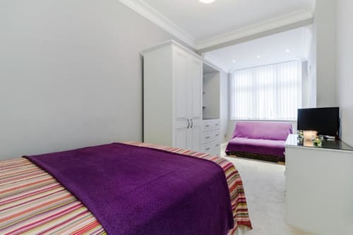 Deluxe Queen Room at Brooklyn House Southgate London, featuring purple bedding, white wardrobe, flat-screen TV, and garden