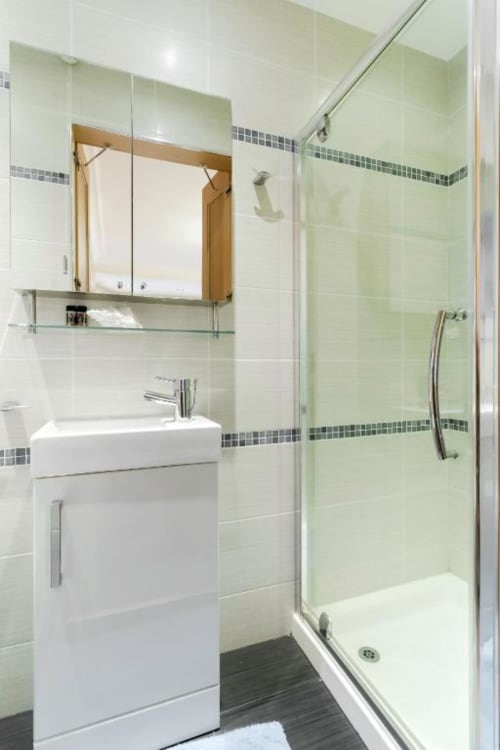 Modern bathroom in Brooklyn House Deluxe King Room with white sink vanity, mirrored cabinet, green tile shower enclosure, and