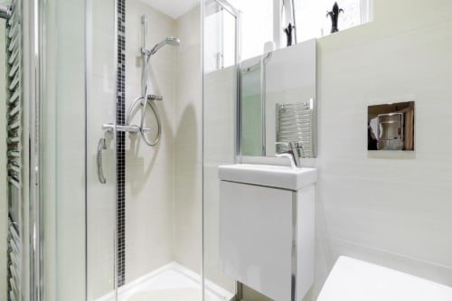 Modern bathroom in Brooklyn House Deluxe Queen Room with walk-in shower, white sink, mirror, and heated towel rack in