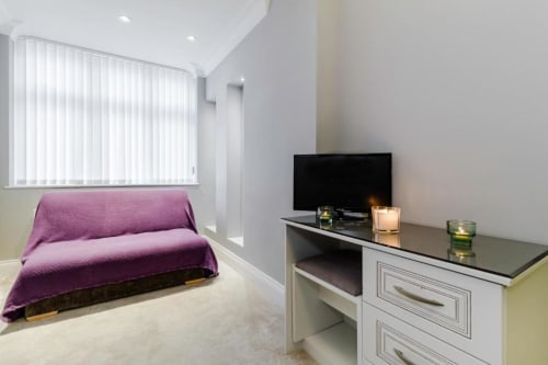 Deluxe Queen Room at Brooklyn House in Southgate, London with purple sofa, TV desk, and garden view through vertical blinds