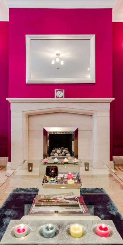 Vibrant magenta fireplace lounge with white mantel, mirror, clock, lit candles, and decorative trays in Brooklyn House Deluxe