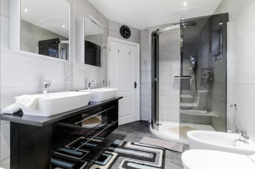 Modern bathroom at Brooklyn House Southgate with dual sinks, walk-in shower, black tile flooring and mirrored vanity