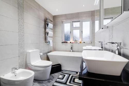 Modern bathroom at Brooklyn House BnB in Southgate, London with white tiles, dual sinks, toilet, and freestanding bathtubs
