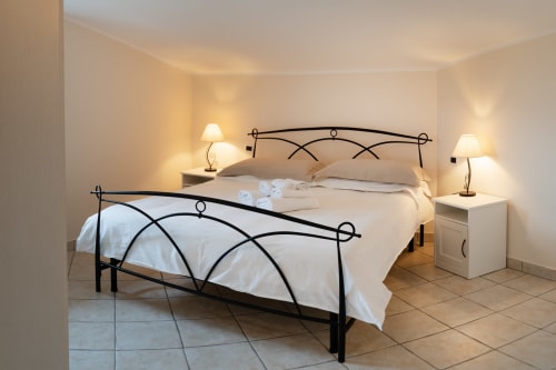 Spaziosa camera da letto presso Villa Del Sole Inn a Campobasso con letto in ferro battuto, biancheria bianca, lampade comodino e pavimentazione in piastrelle