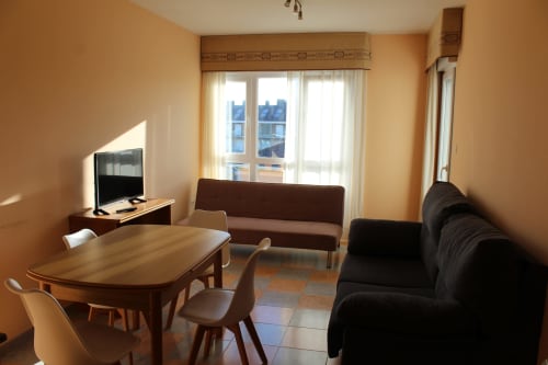 Luminoso salón en Apartamentos Los Gemelos, Foz, con comedor, sofás, TV y balcón con vistas a la ciudad