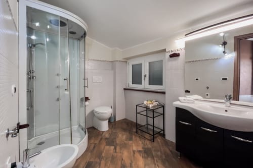 Bagno moderno della Villa Del Sole Inn a Campobasso con doccia in vetro curvo, lavabo curvilineo, pavimento in legno e piastrelle bianche