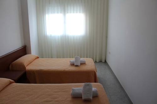 Habitación doble con ropa de cama naranja y toallas enrolladas en Apartamentos Los Gemelos, Foz